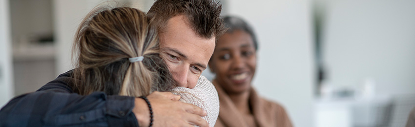 Two adults hugging while a counsellor smiles in the background