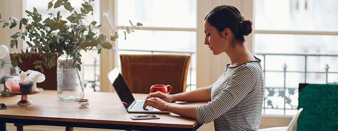 A writer works on her laptop at her kitchen table