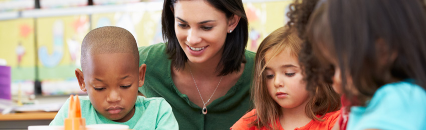 Education assistant works with three children in a classroom setting