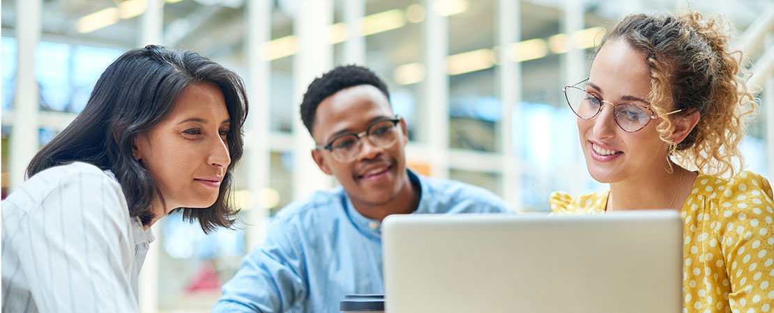 A group of professionals in a modern building looking at a laptop.