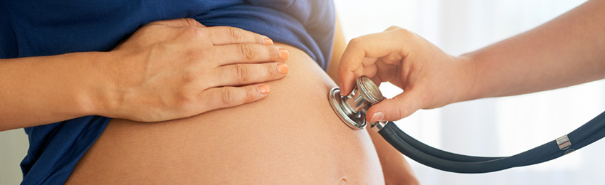 Close-up of a hand holding a stethoscope on a pregnant belly