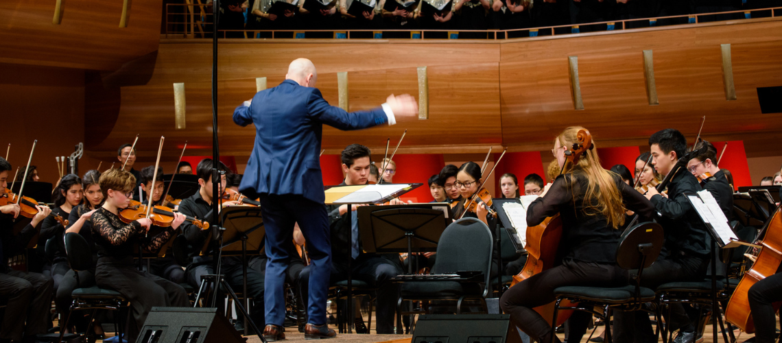 Conductor on stage conducting a youth orchestra and choir