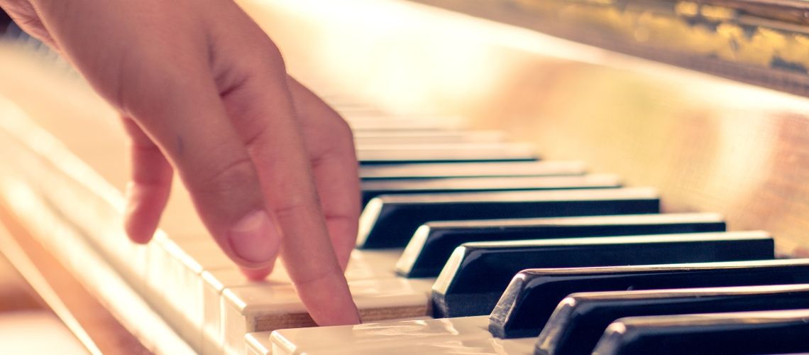 A person’s hand pressing individual keys on a piano