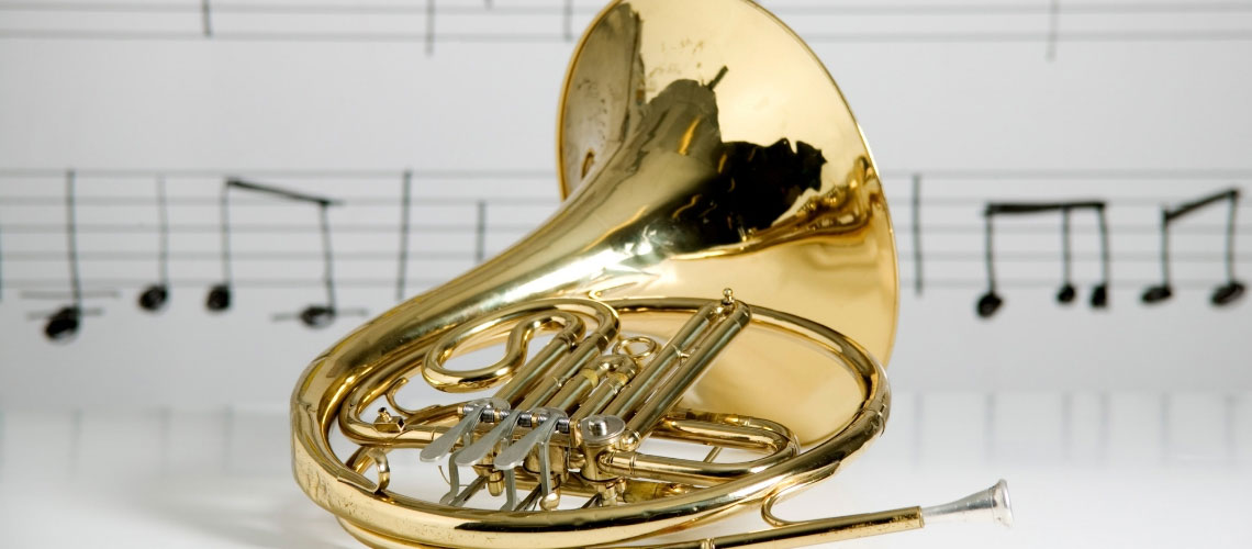 A French horn displayed on it’s side with sheet music behind it