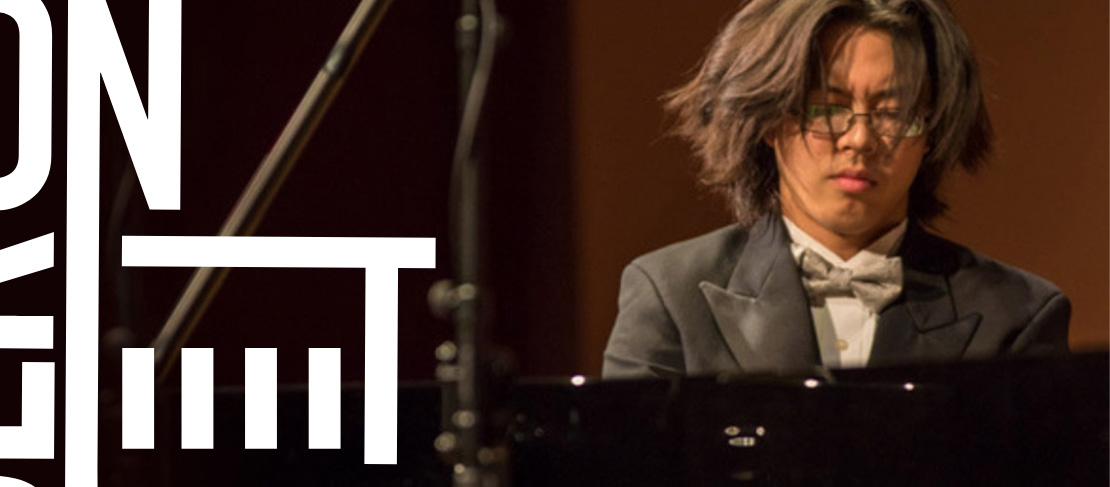A pianist in a tuxedo and bow tie intensely playing a grand piano on stage.