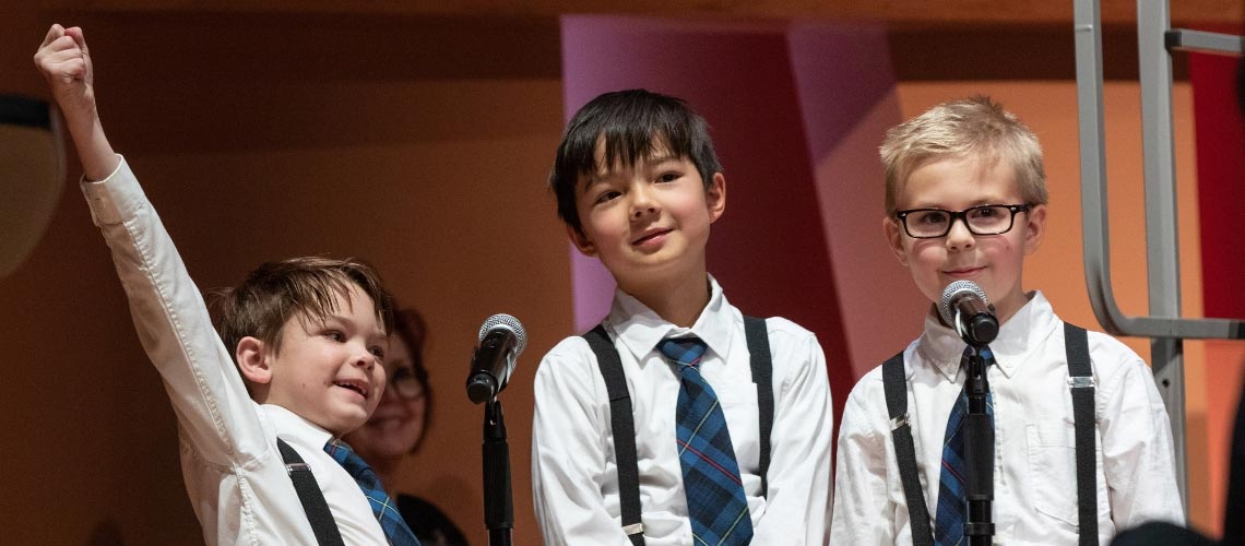 Three young boys standing behind microphones on stage